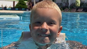 Happy little boy in swim vest life jacket for kids learning to swim in resort hotel pool in summer. Cute little child in float lifejacket swimming in outdoor pool.