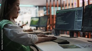 Female Asian Game Programmer Coding On Desktop Computer In Game Development Studio Diverse Office. Focused Woman Writes Lines Of Code, Does AI Engineering For New Immersive 3D Survival Video Game.