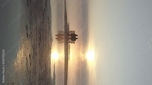 Vertical video. Couple in love sitting on a bench in the middle of the lake and meet the sunrise. The man puts his hand on the woman's shoulder. Flying over people and reflecting lovers in the water.