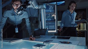 Futuristic Robotic Arm Moving and Placing a Metal Object. Senior Engineer Talks Through This Advanced Process. They are in a High Tech Research Laboratory with Modern Equipment.