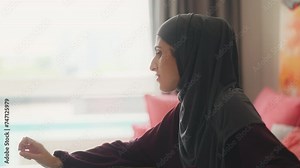 Muslim woman in hijab studying on laptop, writing down task, distance education
