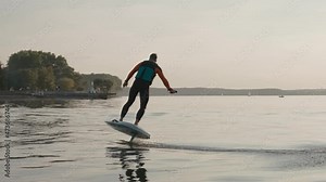 Man rides and falls fromf hydrofoil surfboard on large lake at golden sunset. Shot of man falling from hydrofoil surfboard near lake shore and marina. High quality 4k footage