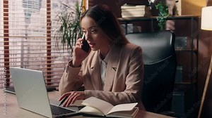 Busy multitasking Caucasian businesswoman female girl lady business woman office worker secretary manager talking mobile phone call writing notes diary report checking information data laptop indoors