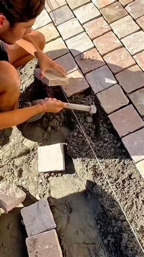 Worker carefully installing cobblestone pavers using hammer and string