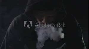 man in black hoodie smoking vape in dark room. blowing smoke
