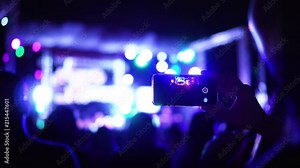 Asian woman person recording video with her phone in concert party with crazy flashing lights show and band on stage.