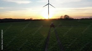 Aerial footage of tractor with fertilizer spreader at spring at sunset.Aerial shot following a tractor spraying field against diseases.Tractor on agriculture field with wind turbine.Renewable energy.