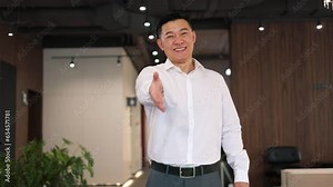 Contented businessman standing in hall of corporate building and reaching out hand for handshaking. Positive asian developer implementing successful deal with investor for construction of new complex.