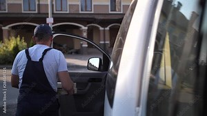 Back view of delivery man in cap and overalls taking two pizza boxes out from van and carrying order to client living in townhouse. Adult worker of delivery service in uniform delivering pizza at home