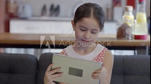 Beautiful little girl playing online games on tablet computer while sitting on sofa at home.Young generation and modern technology usage, education application and lifestyle concept.Slow motion video.