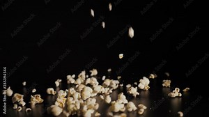 Popcorn falling close up. White pieces of popcorn fall in slow motion a black background and bounce off each other. Closeup.