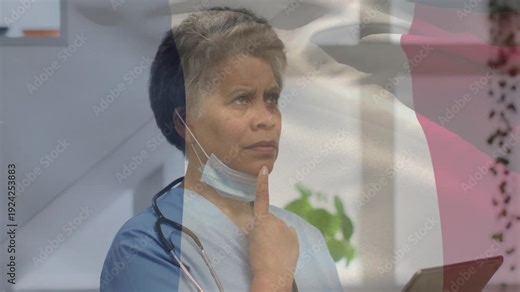 Female MD lowering gaze and tapping tablet in clinic updating chart while flag rippling across face