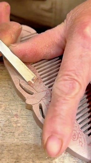 carving intricate ornamental patterns on a wooden comb using a sharp metal hand chisel carefully