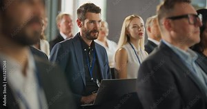 Caucasian Man Sitting in a Crowded Audience at an IT Conference. Delegate Using Laptop Computer to Take Notes. Software Developer Watching Presentation About New High Tech Products and Cloud Solutions