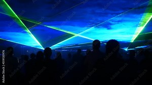 A modern laser light show, with a projection on smoke, a crowd of people watches the laser beams that turn into various lines and shapes. Outdoor performance.