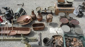 A collection of antique bronze pots, metal weighing scales, and other curiosities displayed at a flea market in Spain
