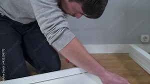 Moving in new house. Unpacking boxes and assembling furniture. Man reading instruction and assembly furniture. DIY. Male installing new white furniture. Do it yourself. Furniture assembly process