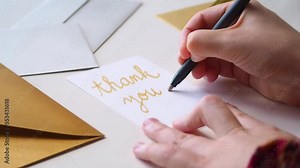 Close up of person writing thank you card by hand with calligraphy pen, in golden cursive letters. On the desk, fancy silver and gold envelopes are ready for sending a message of gratitude for a gift Stock Video