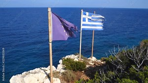 The damaged flag of the European Union and the broken Greek flag waving in the wind on a cliff with the sea in the background