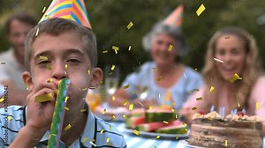 Boy blowing party horn with confetti animation over family gathering outdoors