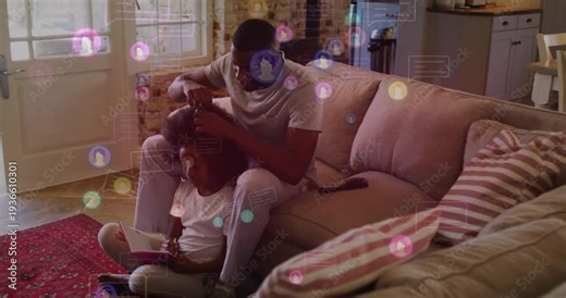Dad reaching, combing child's hair on sofa, bonding while child using tablet, floating social icons