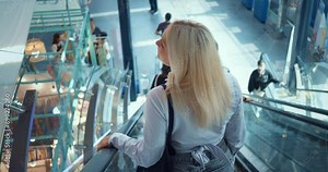 Woman ride down escalator. Back rear view. Woman at airport or train station goes down escalator, looking around. Female traveler tourist arriving by plane in new city town country. Tracking shot