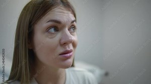 Close-up. A woman's face while measuring body temperature with a non-contact infrared thermometer. The woman is pleased with the result and nods, smiling