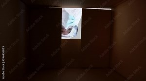 Doctor in protective suit and medical mask opens and close a cardbox during Covid19. Male nurse wearing hand gloves and PPE looking inside carton box at clinic hospital. Coronavirus pandemic concept.