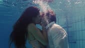 romantic couple kissing underwater in swimming pool wearing clothes...