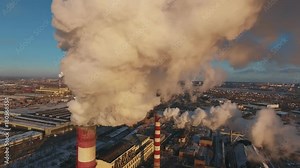 Pipes with smoke: industrial production, plant, air pollution. Dense thick smoke comes from industrial red-white pipes: from a bird's eye view. Industrial zone: smoke comes from the pipe.