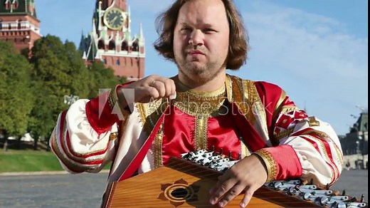 Folk musician in traditional Russian clothes plays an old Russian musical instrument gusli on the background of the Kremlin on red Square. Moscow, Russia