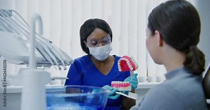 African american dentist demonstrates to patient how to properly brush teeth