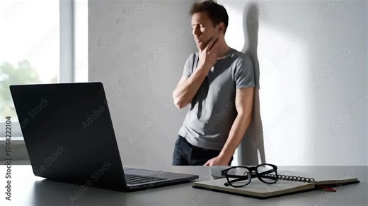 A stressed man experiencing burnout recovery sitting at a desk with a laptop and notebook in a bright office