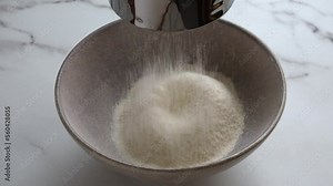 Wheat flour sifting through a metal sieve and pouring into ceramic mixing bowl. Shortcrust pastry preparation. Ingredients for shortbread dough. Close up. Marble background