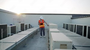 Utility engineer sitting near compressor recheck refrigeration system of the factory and system operation. Maintenance operator inspecting the air conditioning system on the roof deck of the factory