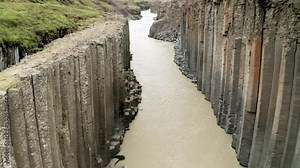 Studlagil columnar basalt canyon in the Eastfjords of Iceland, with milky coloured glacial river, high cliffs and grass fields.