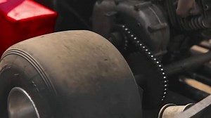 Close-up of the motor, transmission and smooth tire of the go-kart, transmission chain and gears are visible.