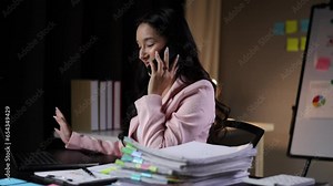 Businesswoman working on paperwork and talking to partner on mobile phone while reading and analyzing monthly work schedule.