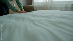 A housekeeper in a uniform makes a bed preparing a luxury hotel room for guests cleaning and travel concept
