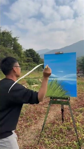 Artist painting a blue landscape outdoors using green grass blades