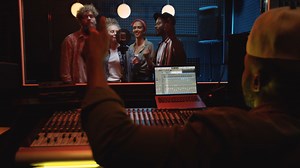 Rear Of The Man Sound Engeneer Sitting At The Sound Board In The Dark Studio And Mastering The Song While Male And Female Four People Group Singing Together And Recording At The Microphone | Free Stock Video Footage