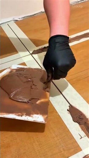 filling gaps between the wooden floor tiles with brown grout using a flat tool for clean surfaces
