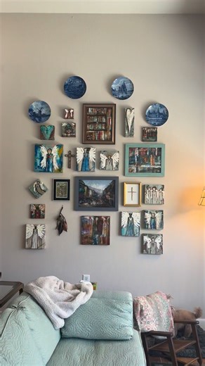 Sara Thurman | Coach Mentor on Instagram: "Y’all, my Man put this together for me today in our new sitting space looking out our gorgeous picture window to wildlife and birds and an in-ground stream. These pieces of art are mostly created by me the last nine years but some are from the country of Georgia, crosses gifted to me and an encaustic basket wall hanging with cooper leaves by Matt Tommey. #gallerywall #angels #tellingstories #myhappyplace"