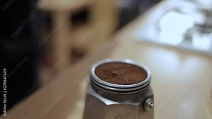 A funnel filter filled with grounded coffee being placed into the valve of a coffee moka pot.