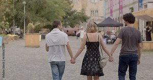 Girl and two guys, back view. Urban environment. Romantic relationships among three individuals polyamory, involve consensually and openly loving and connecting with multiple partners simultaneously.