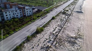 An aerial view of the boardwalk at Rockaway Beach in Queens, NY on a sunny day. The drone camera dolly in and pan right, following behind a peloton of eight cyclists enjoying the beautiful day.
