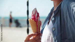 a girl eats ice cream in a cone on the beach. a girl goes with an ice cream cone on the beach. close-up of lips with strawberry ice cream. hot summer. melted ice cream flows down the arm