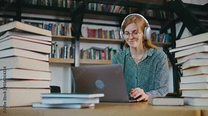 Young girl college student sit at desk use pc laptop computer watching distance online learning seminar class remote university webinar having virtual classroom meeting in library. Woman in headphones