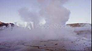 Water steam rising and water eruptions at El Tatio Geyser Field with mountains in the background. Third-largest geyser field in the world.