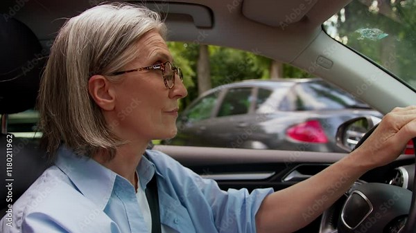 Focused elderly Caucasian woman in glasses mature senior female automobile driver driving auto car steering wheel riding vehicle fast speed road way rental service fasten seat belt in machine motorcar